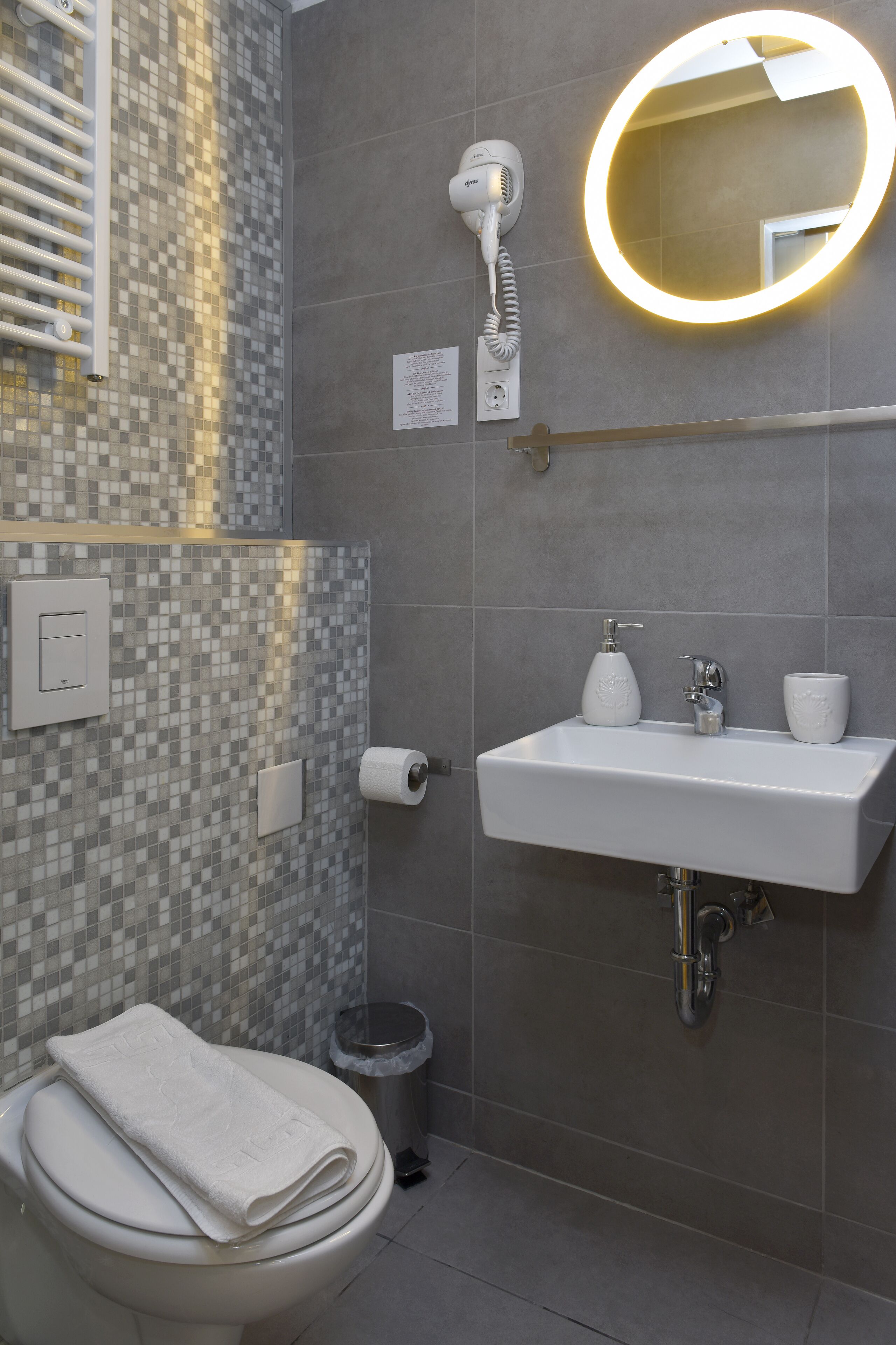 Un baño con inodoro, lavamanos y secador de pelo fijado a la pared.