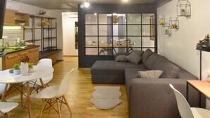 A modern living space with a dining area, a grey sofa, and a kitchen visible through a large window. - Walk Inn Váci 78 (Budapest)