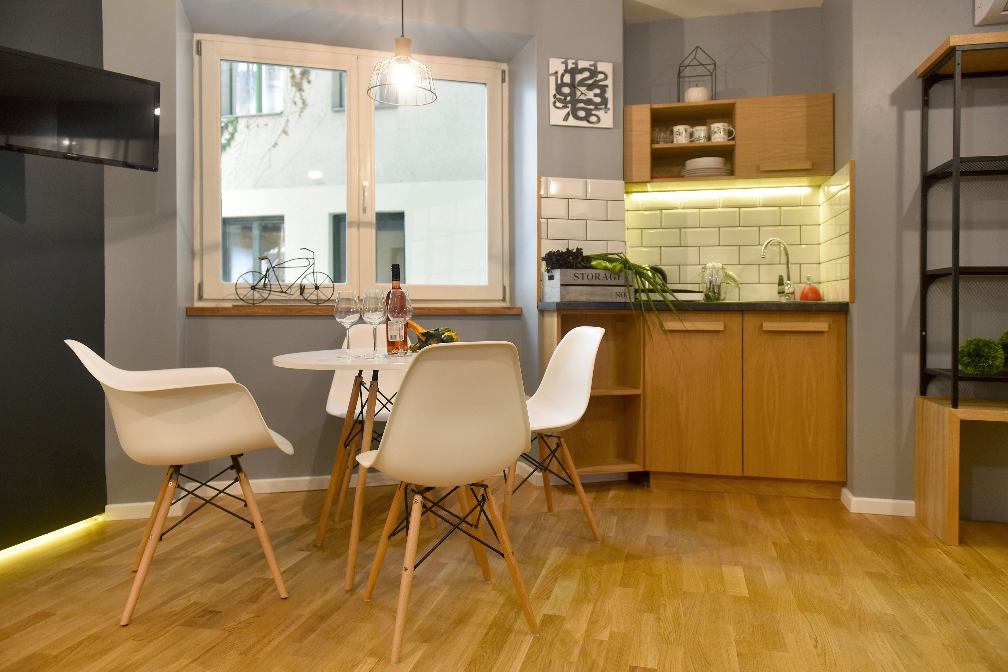 A modern kitchen with wooden cabinets, a tiled backsplash, and a dining area with white chairs and a wooden table.