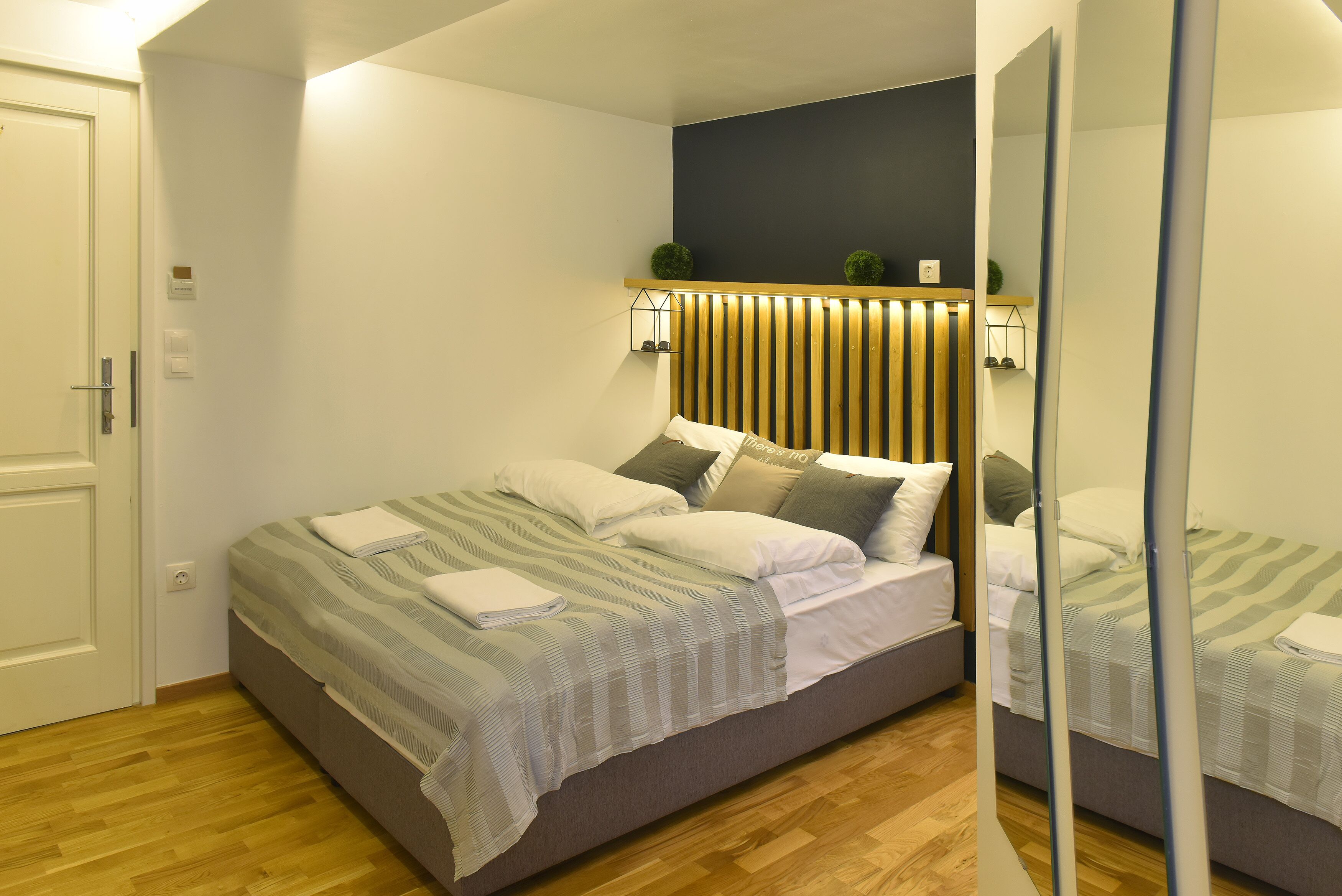 Un dormitorio moderno con cama, cabecero de madera, lámparas de noche y un espejo.