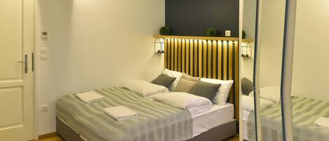 Un dormitorio moderno con cama, cabecero de madera, lámparas de noche y un espejo.