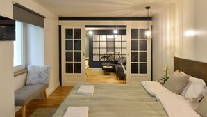A bedroom with a large bed, a bench, and a view into a dining area. - Walk Inn Váci 78 (Budapest)