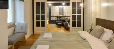 Een slaapkamer met een groot bed, een bankje en uitzicht op een eetruimte.