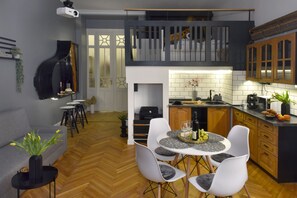 A modern kitchen with a dining area, a staircase leading to an upper level, and a piano in the living area.