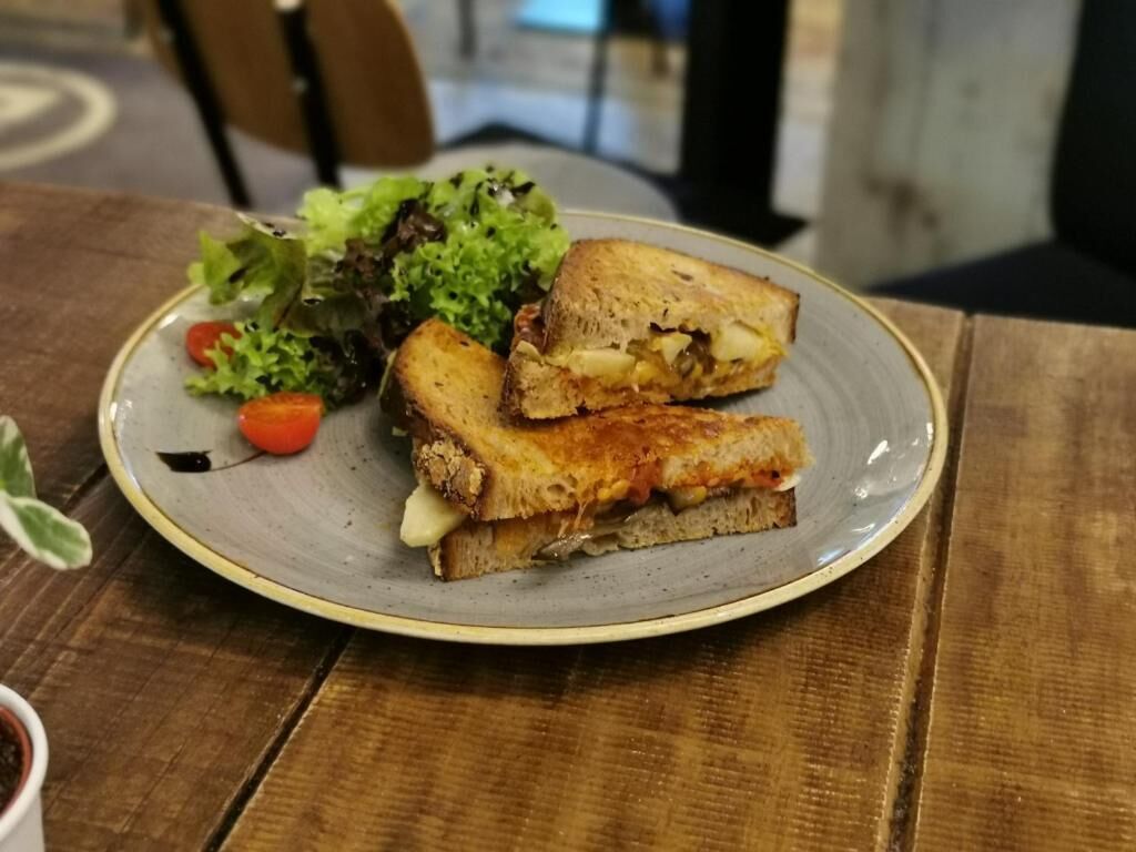 A plate with a grilled sandwich, a side salad, and a small tomato on a ceramic plate.