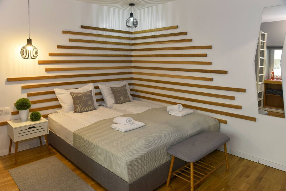 Un dormitorio moderno con una cama grande, listones de madera en la pared, una mesita de noche con lámpara y un banco.