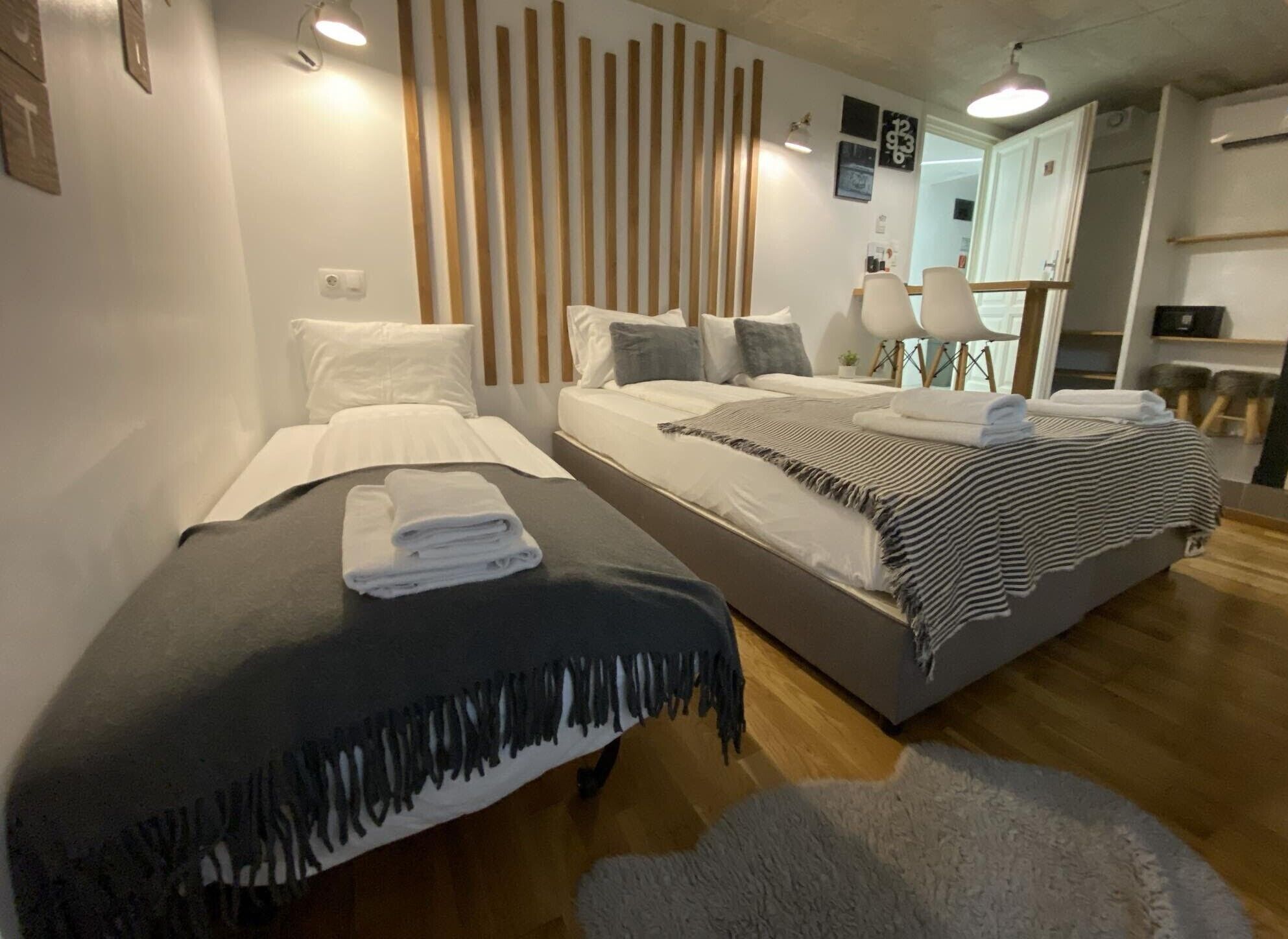 A modern hotel room with two beds, a wooden slat wall, and a small desk area.
