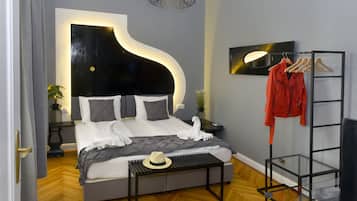 A modern bedroom with a curved headboard, a bed with white linens, a bedside table with a hat, and a coat rack with a red jacket.