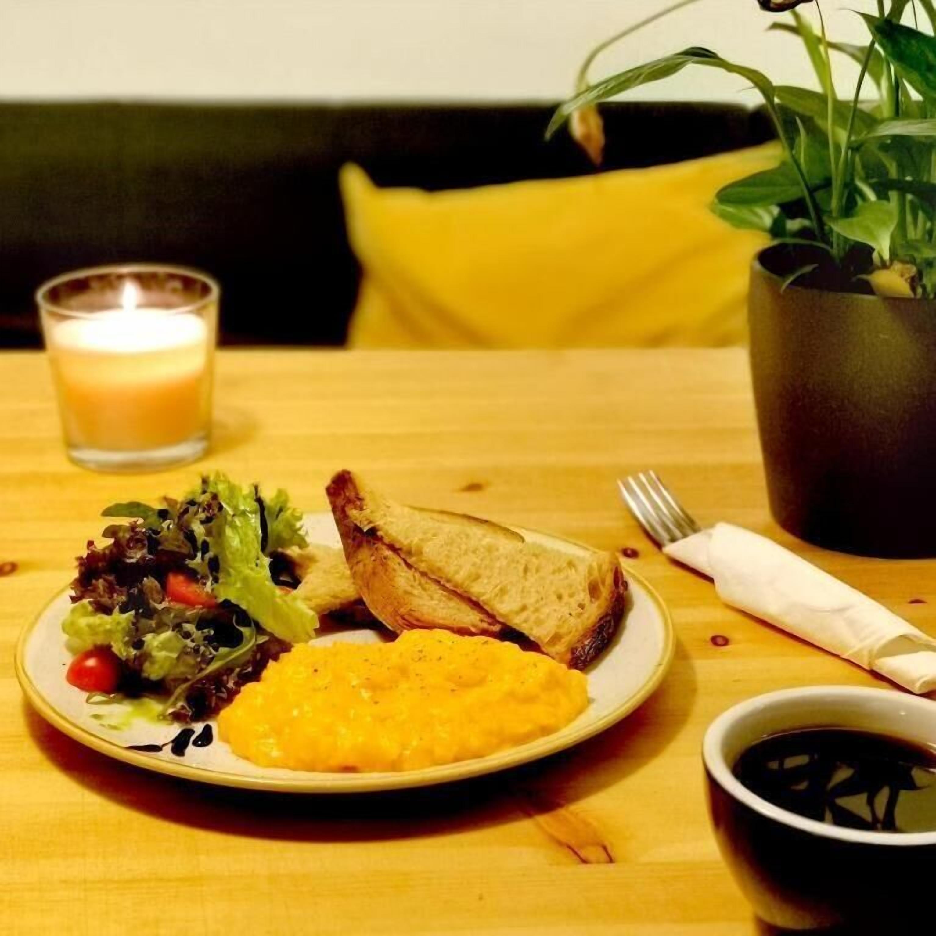 Una mesa de comedor con un plato de comida, una vela, una planta y una taza de café.