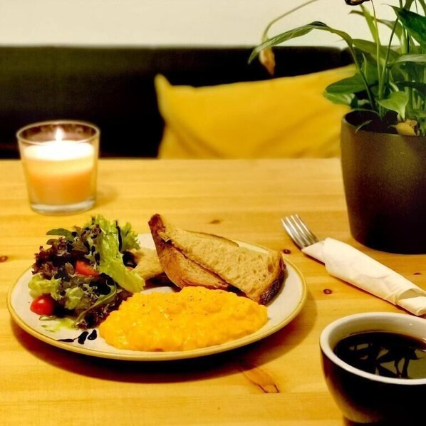 A dining table with a plate of food, a candle, a plant, and a cup of coffee.