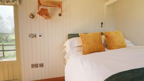 Une chambre avec un grand lit, un banc en bois sur lequel sont posés des vêtements, un thermostat et une vue sur l’extérieur.