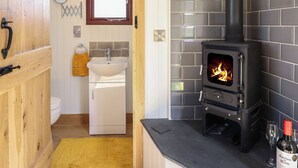 Une salle de bain avec une porte en bois, un lavabo blanc et un poêle noir dont on peut voir le feu.