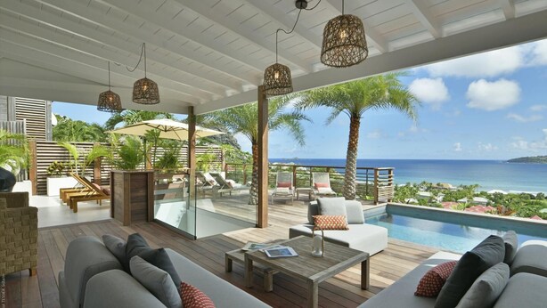Un espace de détente extérieur moderne, doté d’une piscine, d’une terrasse en bois et de différents coins salon offrant une vue sur l’océan.