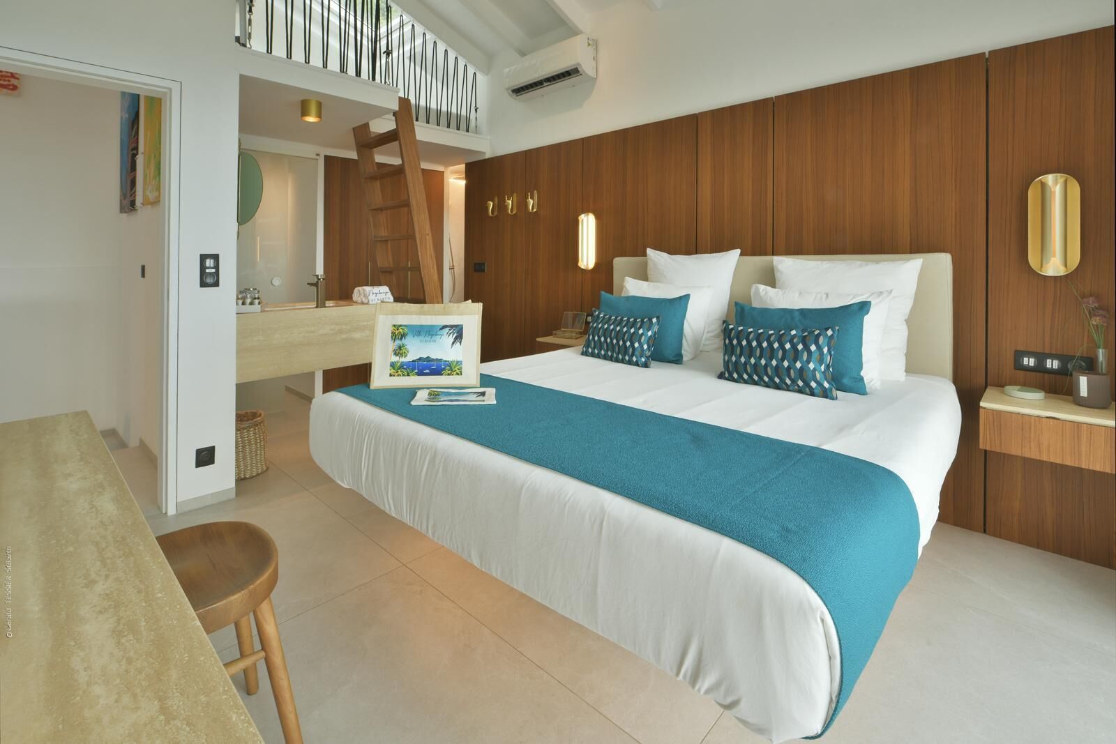 Une chambre d’hôtel moderne avec un grand lit, une armoire en bois, un bureau avec une chaise et une salle de bain visible à travers une porte ouverte.