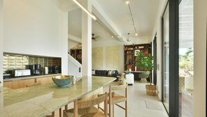 Une cuisine moderne avec une table à manger en verre, des chaises en bois et un grand saladier. Un escalier mène à un espace de vie comprenant un canapé et une table basse.