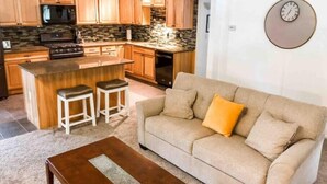 Una cocina moderna con armarios de madera, una isla central con taburetes, horno empotrado y microondas.