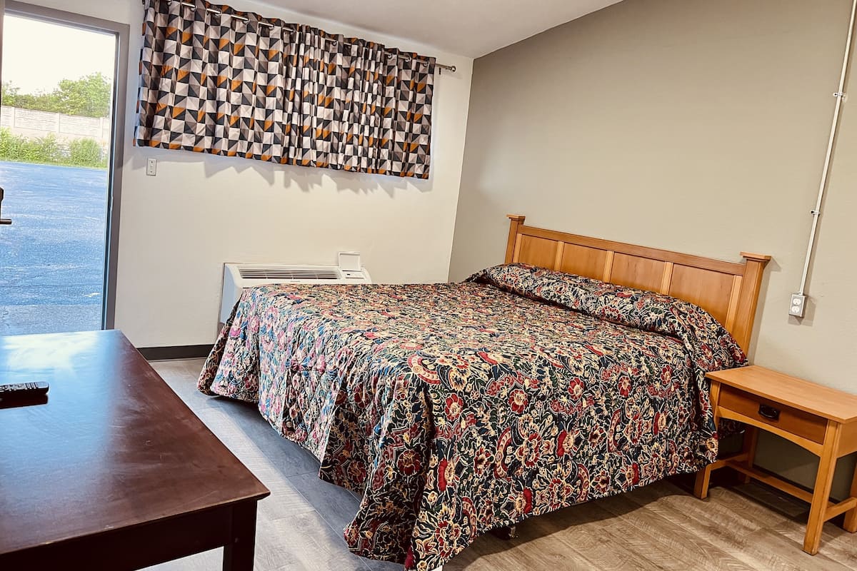 Une chambre à coucher avec un lit, une table de chevet en bois, un bureau et une fenêtre avec des rideaux.