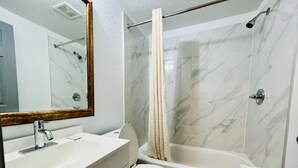 Un baño con pared de mármol, una bañera, un inodoro y un lavabo con espejo.