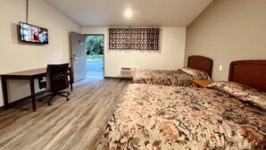 Habitación de hotel con cama, escritorio, silla, televisor y puerta que da a un balcón.