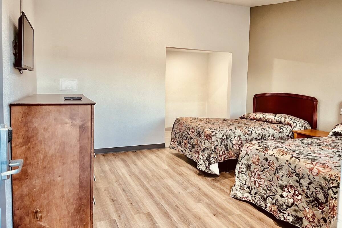 Une chambre d’hôtel avec deux lits, un bureau en bois et un téléviseur fixé au mur.
