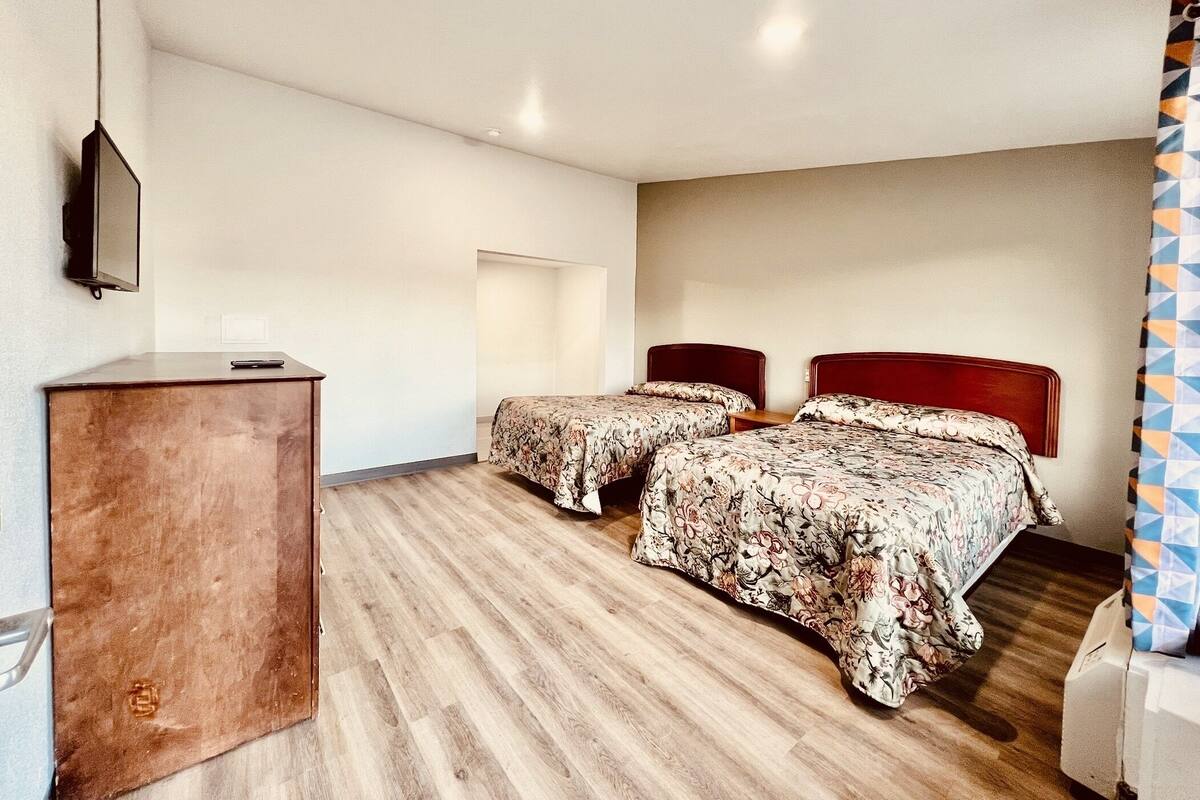 Une chambre avec deux lits, un bureau en bois et un téléviseur fixé au mur.