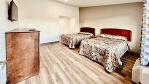 Una habitación con dos camas, un escritorio de madera y un televisor en la pared.