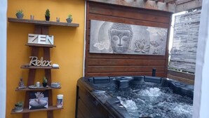 Ett spaområde med ett bubbelbad, trähyllor med växter och dekorationer samt en vägg med en målning av Buddha.
