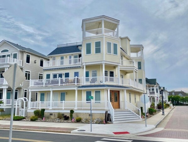 A multi-story residential building with a balcony on the second floor, a front porch, and a visible street sign.