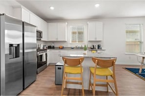 A modern kitchen with white cabinets, stainless steel appliances, and wooden chairs.