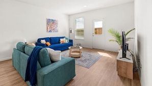 Una sala de estar moderna con un sofá azul, una pequeña mesa redonda de centro y una mesita de noche de madera con una planta.