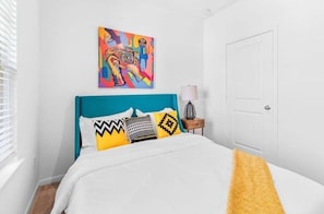 A bedroom with a teal headboard, a colorful abstract painting, and a white door.