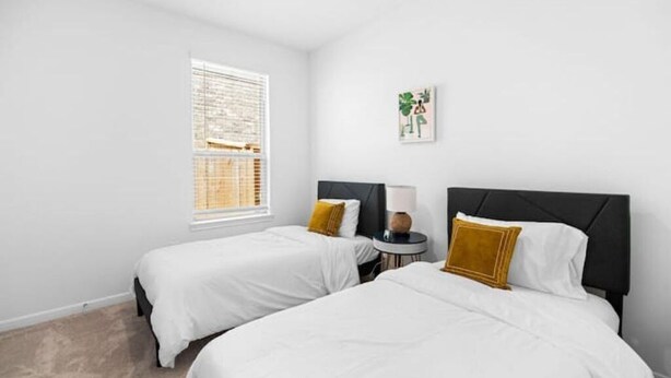 Une chambre d’hôtel avec deux lits, une petite table ronde, une fenêtre avec des stores et une œuvre d’art accrochée au mur.