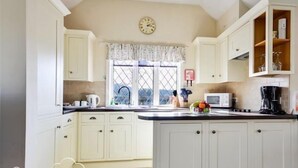 A kitchen with white cabinets, a window with lace curtains, a clock, and a microwave. - Frome Lodge House (Dorchester)