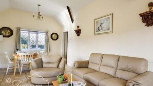 A cozy living room with a beige sofa, a wooden coffee table, and a dining area with a white table and chairs. - Frome Lodge House (Dorchester)