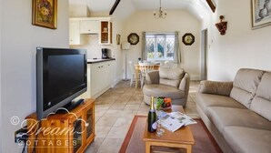 A cozy living room with a television, a sofa, and a coffee table. There is a kitchen area with cabinets and a dining table. - Frome Lodge House (Dorchester)