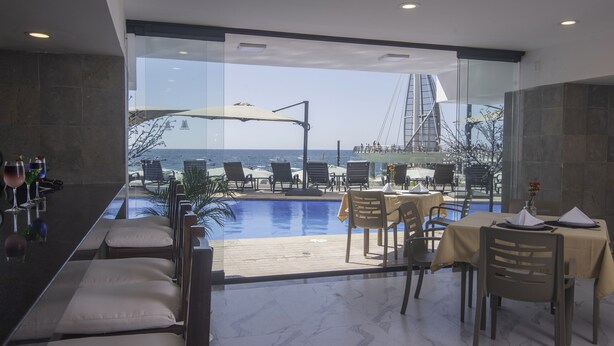 Un área de comedor exterior moderna con piscina, con vista al mar y a un puente.