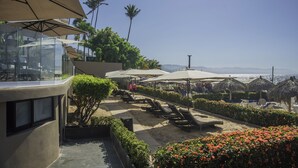 Un resort con terraza al aire libre, palmeras y vista al océano.