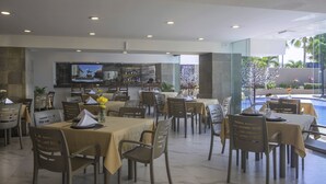 Un restaurante con varias mesas y sillas, una zona de bar y una piscina visible a través de amplios ventanales.