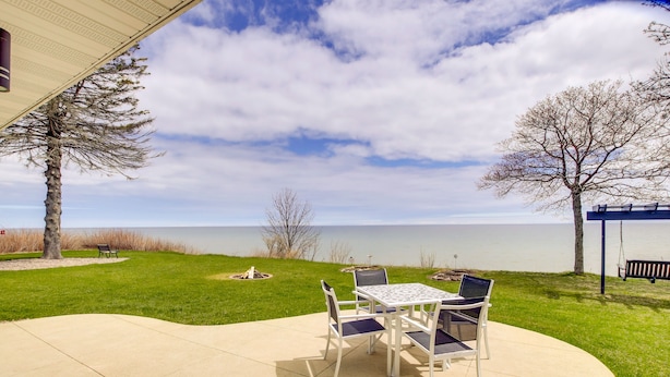 A patio with a table and chairs, a bench, and a view of a lake. - Waterfront Algoma Vacation Rental on Lake Michigan (Algoma)