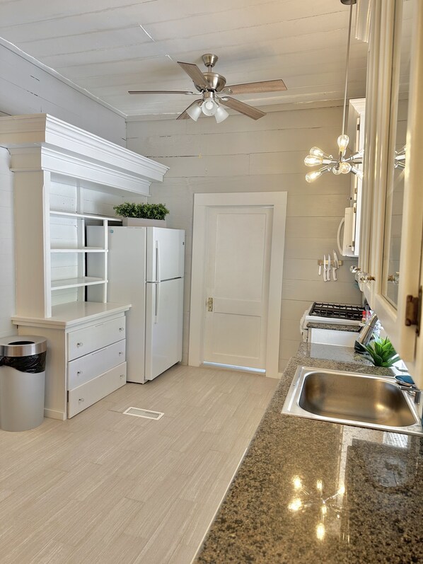 A kitchen with white cabinetry, a stainless steel sink, a ceiling fan, and a plant on the countertop.