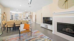 A modern living room with a fireplace, a TV, and a dining area with chairs and a table.