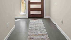 A hallway with a patterned rug, a wooden door, and a hanging light fixture.