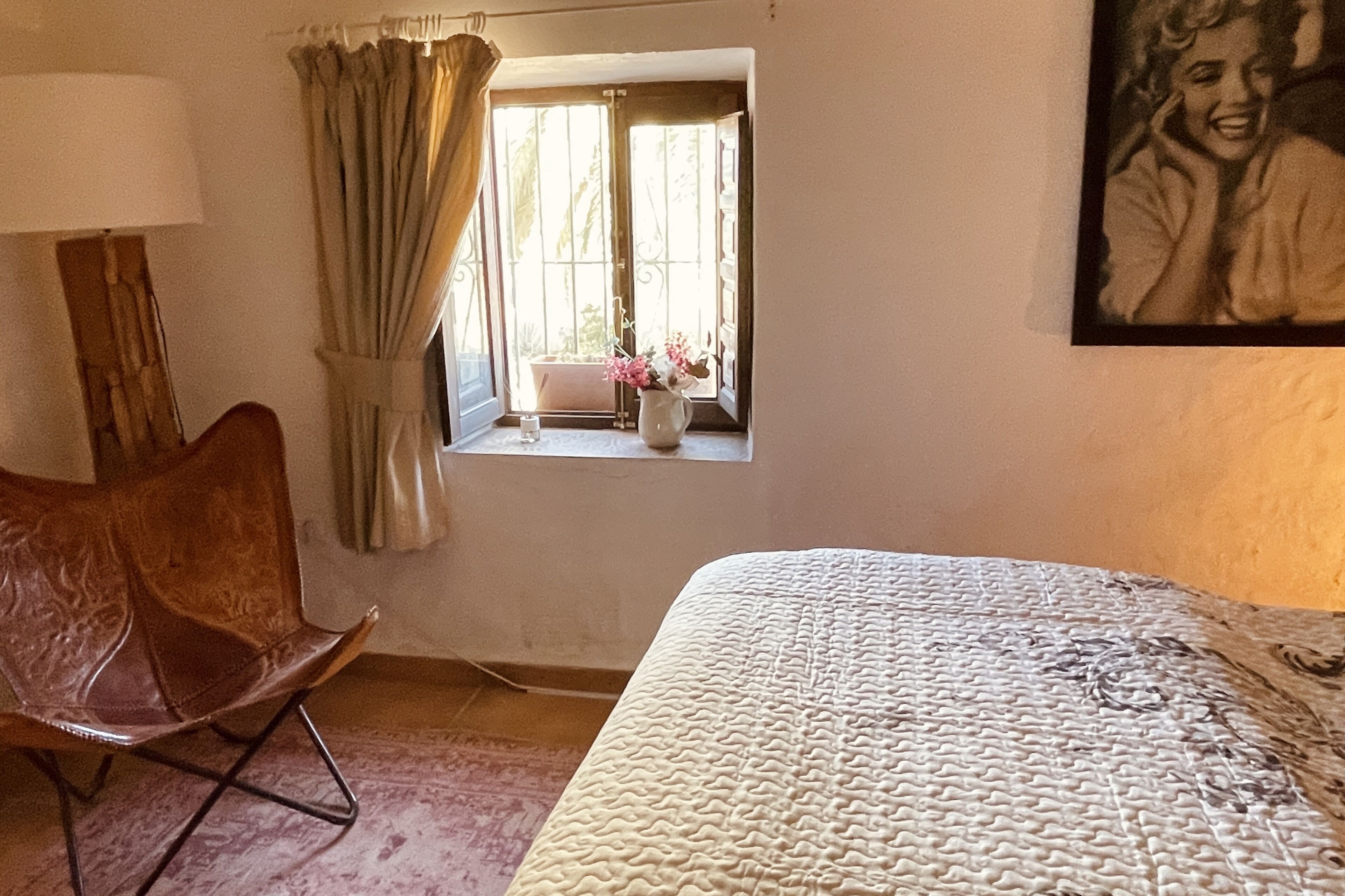 Une chambre à coucher avec un grand lit, une chaise, une fenêtre avec des rideaux et un tableau accroché au mur.