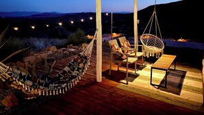 Un patio exterior con terraza de madera, una hamaca colgante y un espacio de descanso con sillas y una mesa.