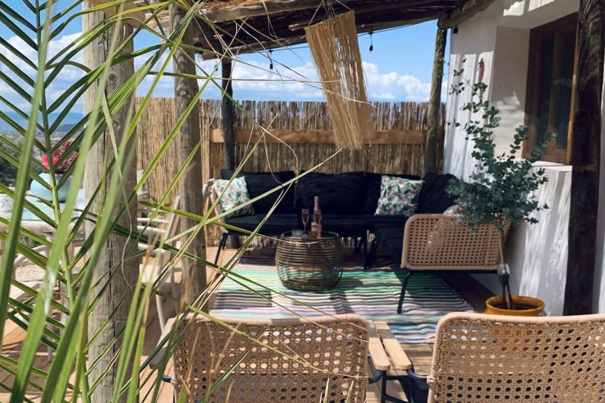 A covered outdoor seating area with wicker furniture, a woven table, and a thatched ceiling.