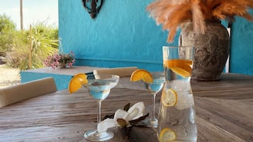 A table with two martini glasses and a large pitcher, both containing a blue liquid and garnished with orange slices.