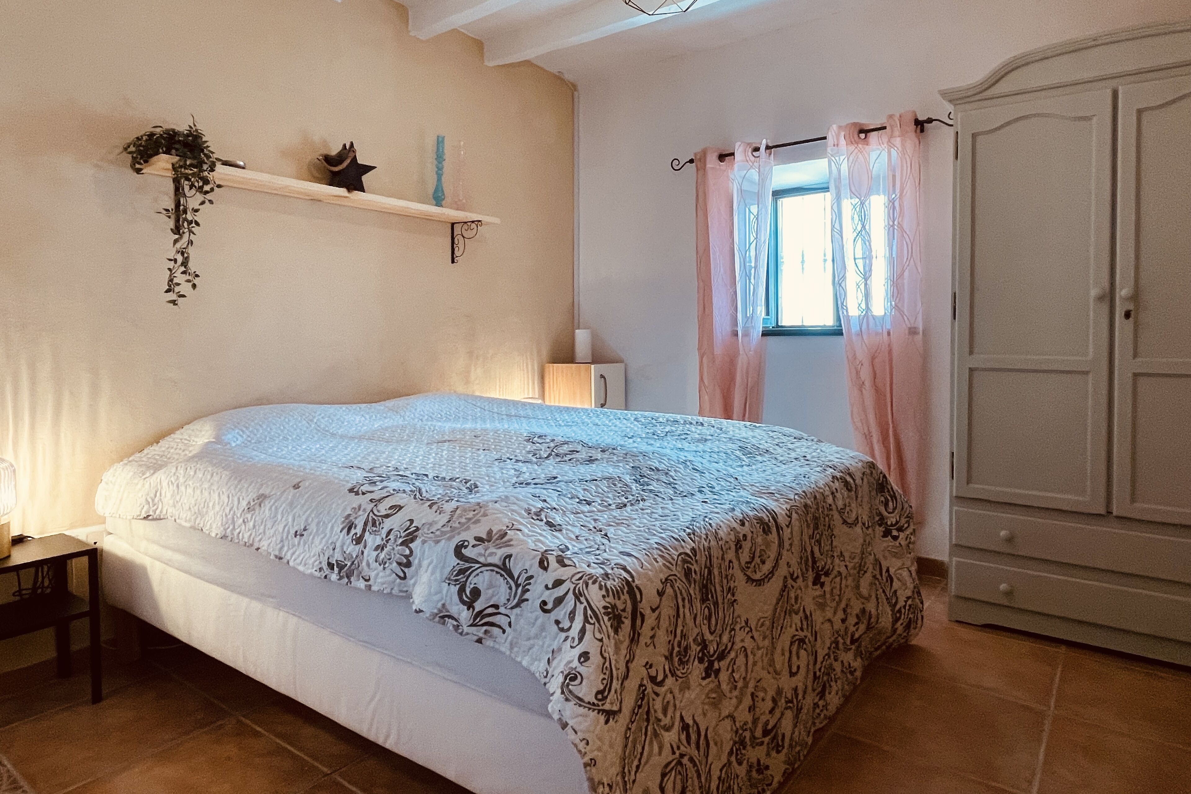 Une chambre à coucher comprenant un lit, une table de chevet, une armoire et une fenêtre avec des rideaux.
