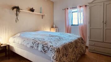 Une chambre à coucher comprenant un lit, une table de chevet, une armoire et une fenêtre avec des rideaux.