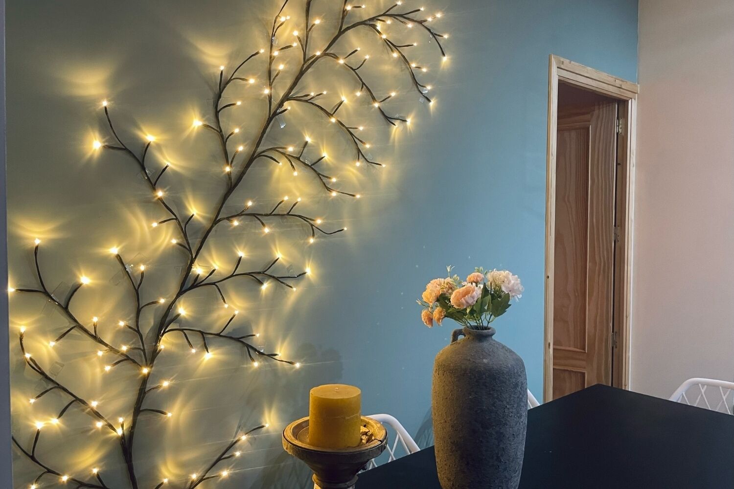 Una habitación con una pared decorada con luces de cuerda, un florero con flores y una vela sobre una mesa.