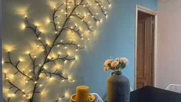 Una habitación con una pared decorada con luces de cuerda, un florero con flores y una vela sobre una mesa.